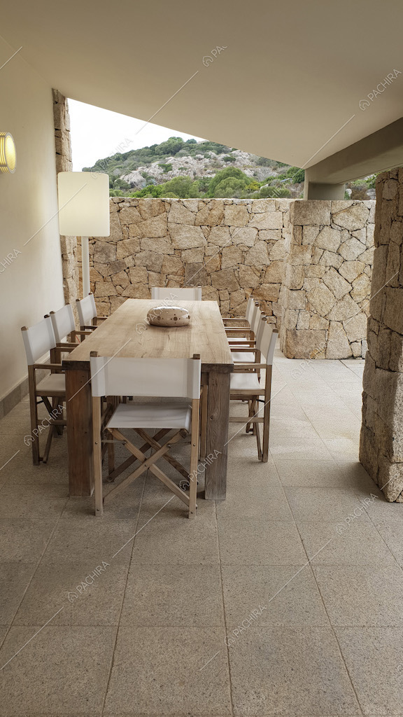 Zona pranzo esterna con tavolo in legno, sedie in tela pieghevoli e muri di pietra