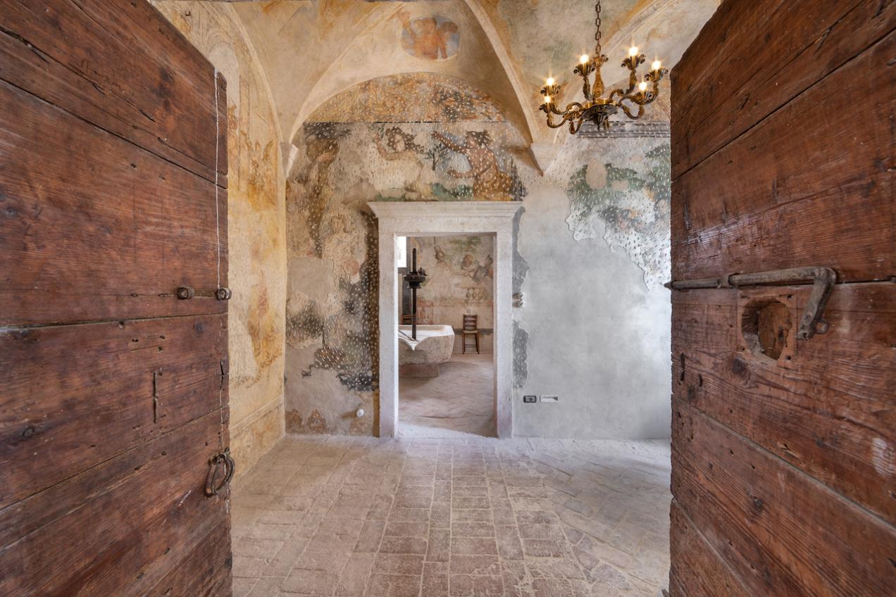 Accesso tramite portone in legno a sala affrescata con pavimento in cotto e vista sulla cucina
