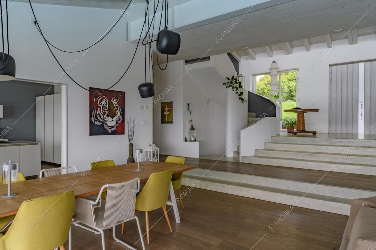 Tavolo da pranzo in legno con sedie bianche e gialle, nella sala dalle pareti bianche con vista su cucina e scale