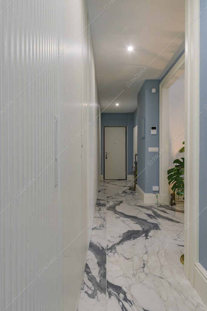 Corridoio con porta scorrevole bianca con boiserie, pavimento in marmo e scorcio sulle piante del salotto