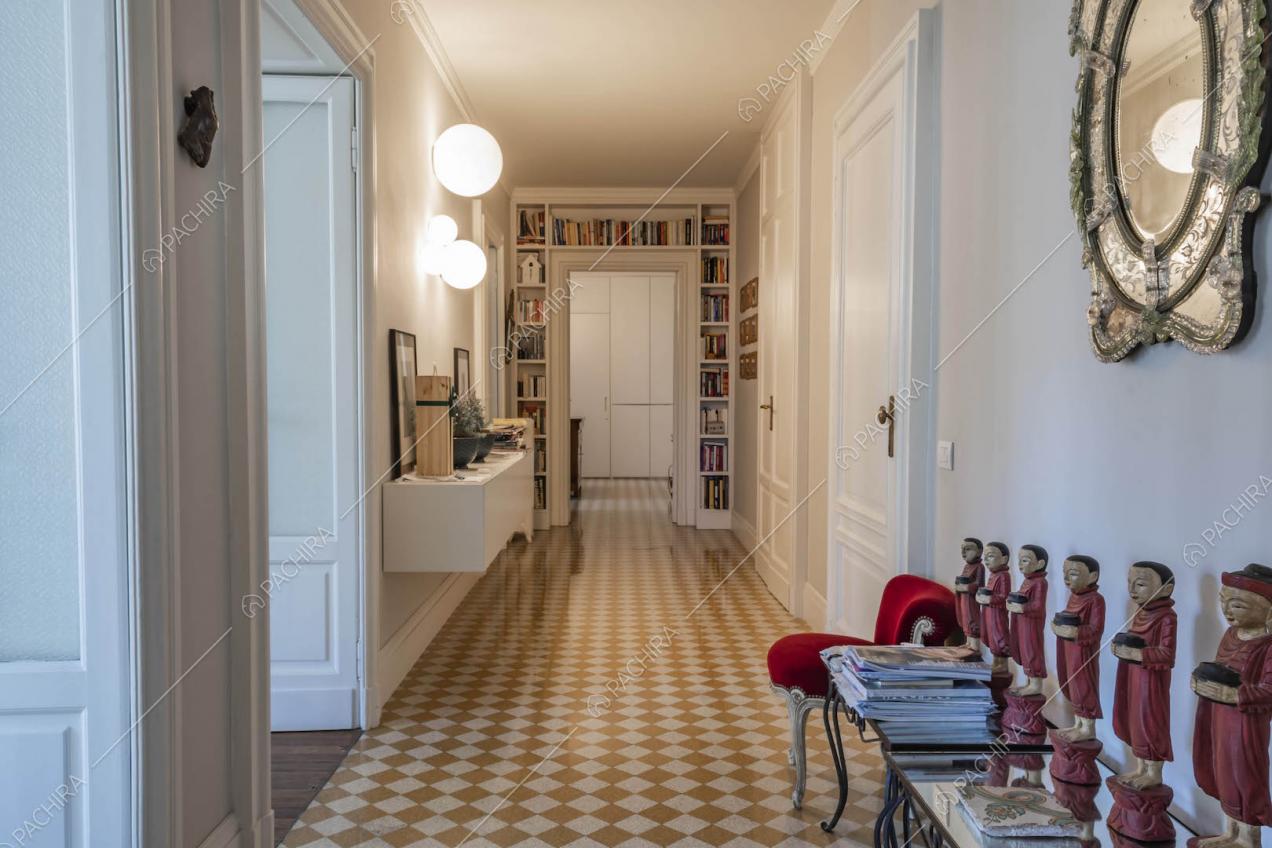 Lungo corridoio con pavimento a scacchi, porte bianche con boiserie e libreria che incornicia la porta