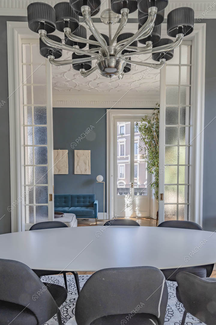 Dal tavolo da pranzo bianco vista sul salotto con boiserie sul soffitto tramite la porta a vetri scorrevole