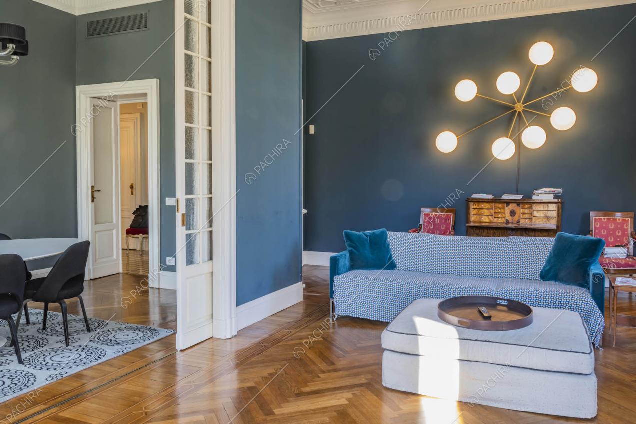 Pouf bianco e divano blu nel salotto con pavimento in parquet e vista sulla sala da pranzo