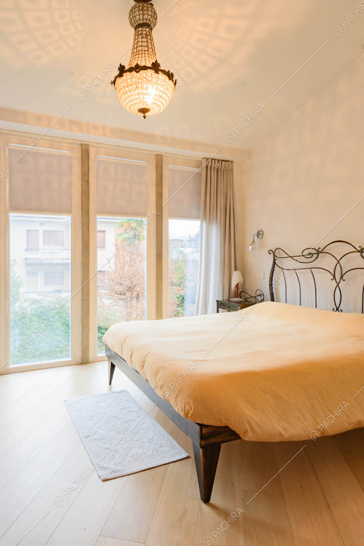 Camera da letto matrimoniale con pavimento in parquet, pareti bianche e grandi vetrate