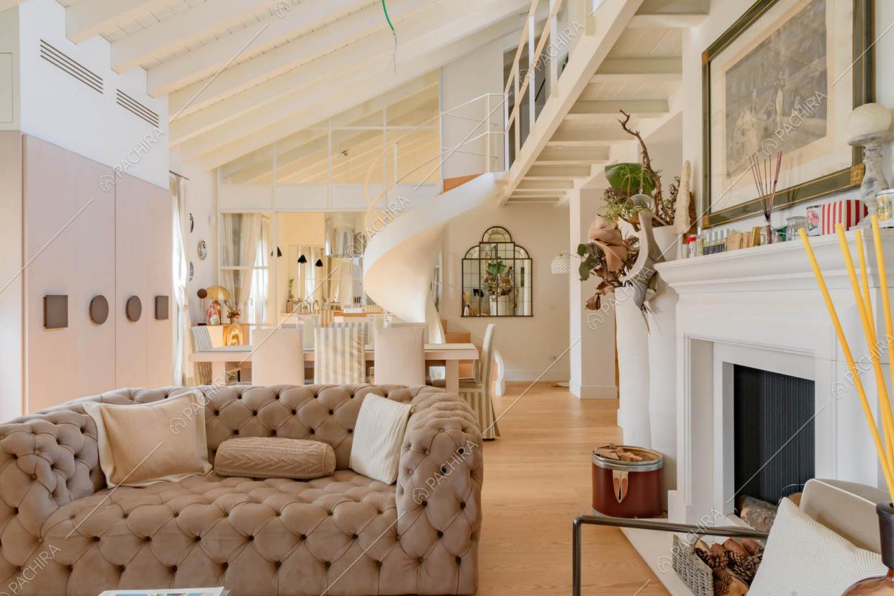 Divanetto beige nella zona living con travi bianche a vista sul soffitto e scala a chiocciola