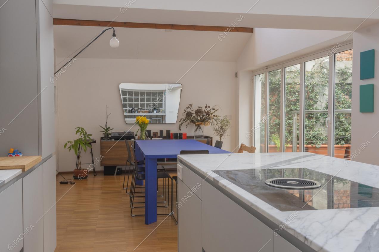 Zona pranzo con parete finestrata e specchio irregolare vista dalla cucina a isola