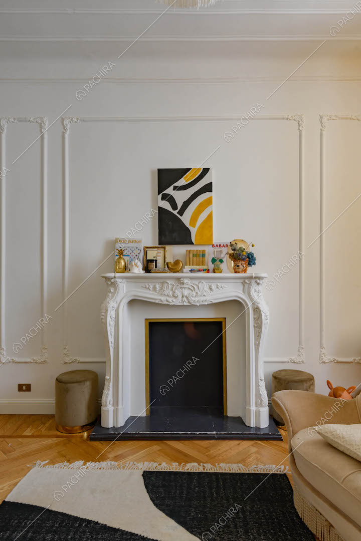 Camino con boiserie sulla cornice bianca, divano e pavimento in parquet a spina di pesce