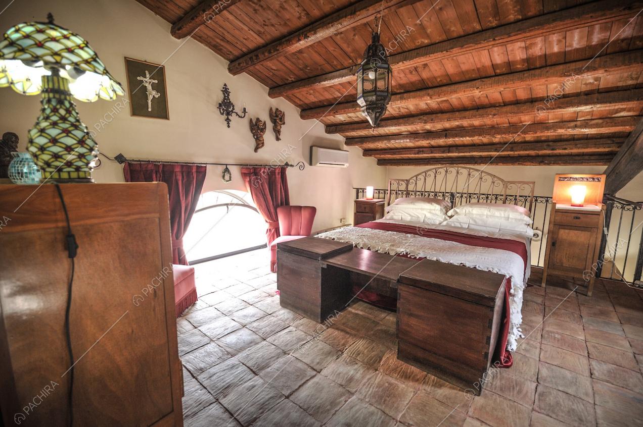 Letto matrimoniale, mobili in legno e poltroncine rosse su pavimento in cotto