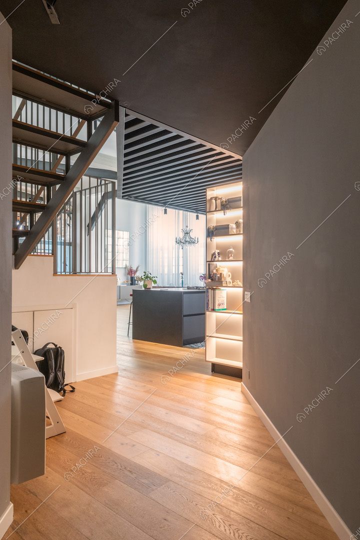 Dal corridoio con pavimento in parquet vista sull'isola nera della cucina, illuminata dalle vetrate in stile industriale