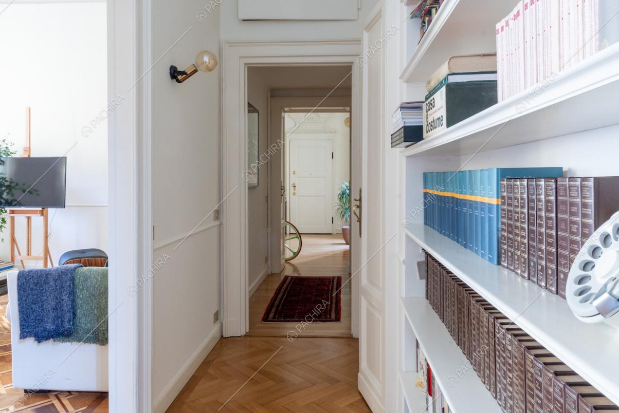Corridoio con pavimento in parquet a spina di pesce, libreria e boiserie alle pareti