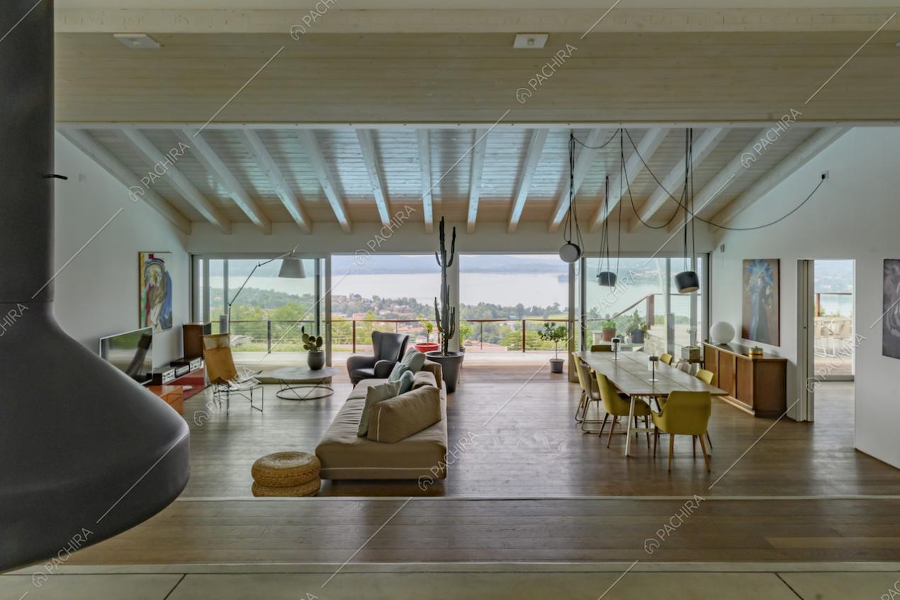 Ampio salotto con pavimento in parquet, camino su un piano rialzato e vetrate con vista sul lago