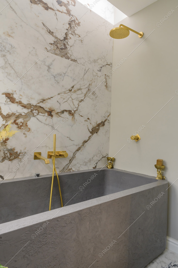 Vasca da bagno grigia con rubinetteria dorata e parete in marmo