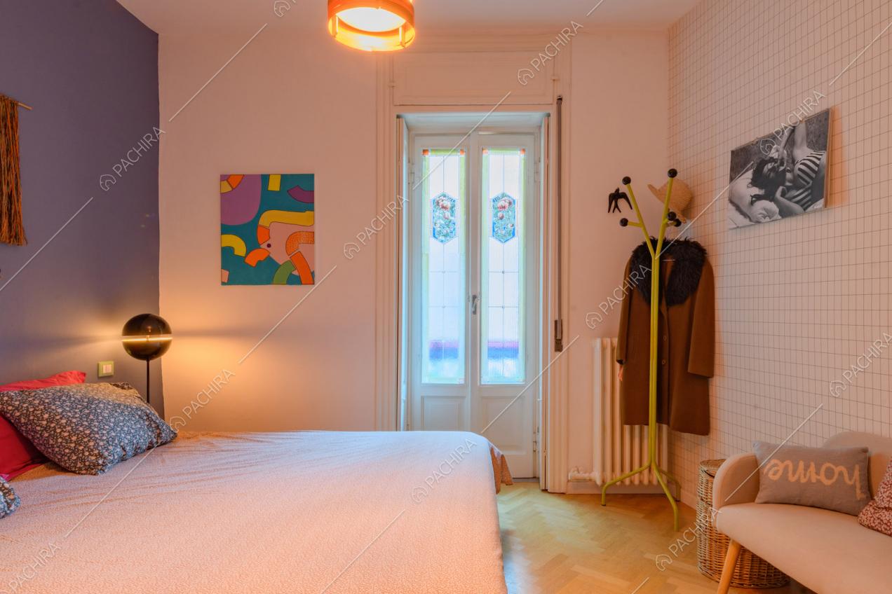 Parete in piastrelle bianche e pavimento in parquet a spina di pesce nella camera da letto matrimoniale