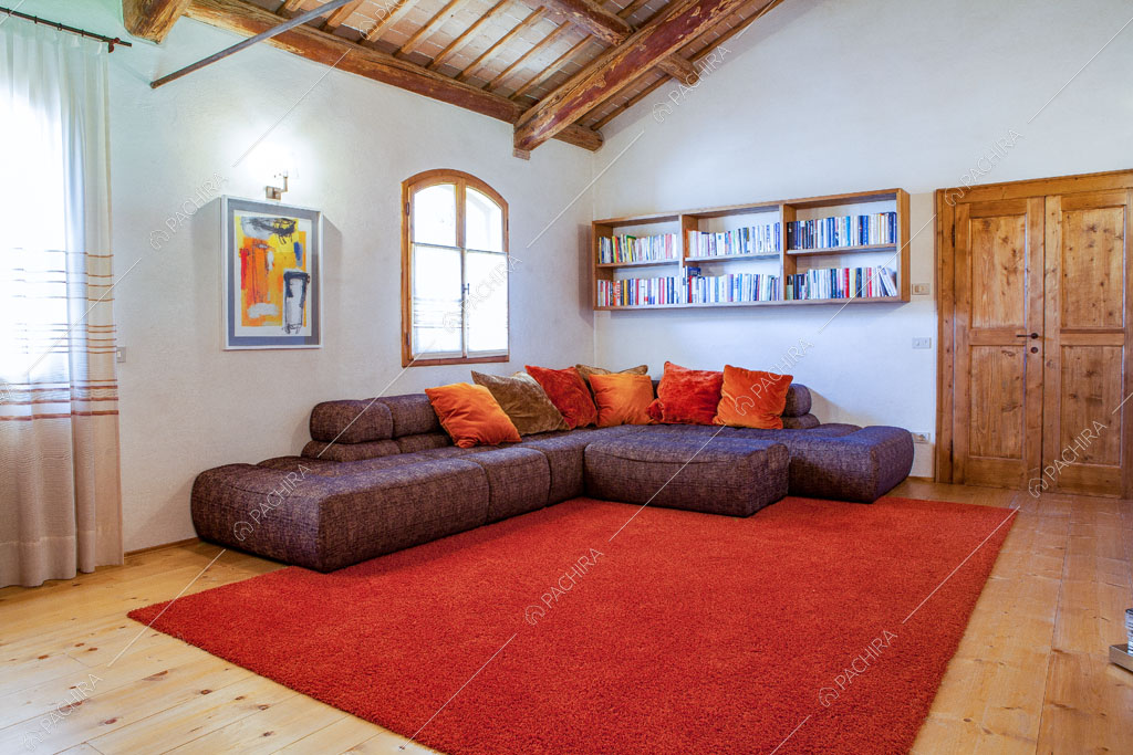 Divano viola nella sala con pavimento in parquet, pareti bianche e travi in legno a vista sul soffitto