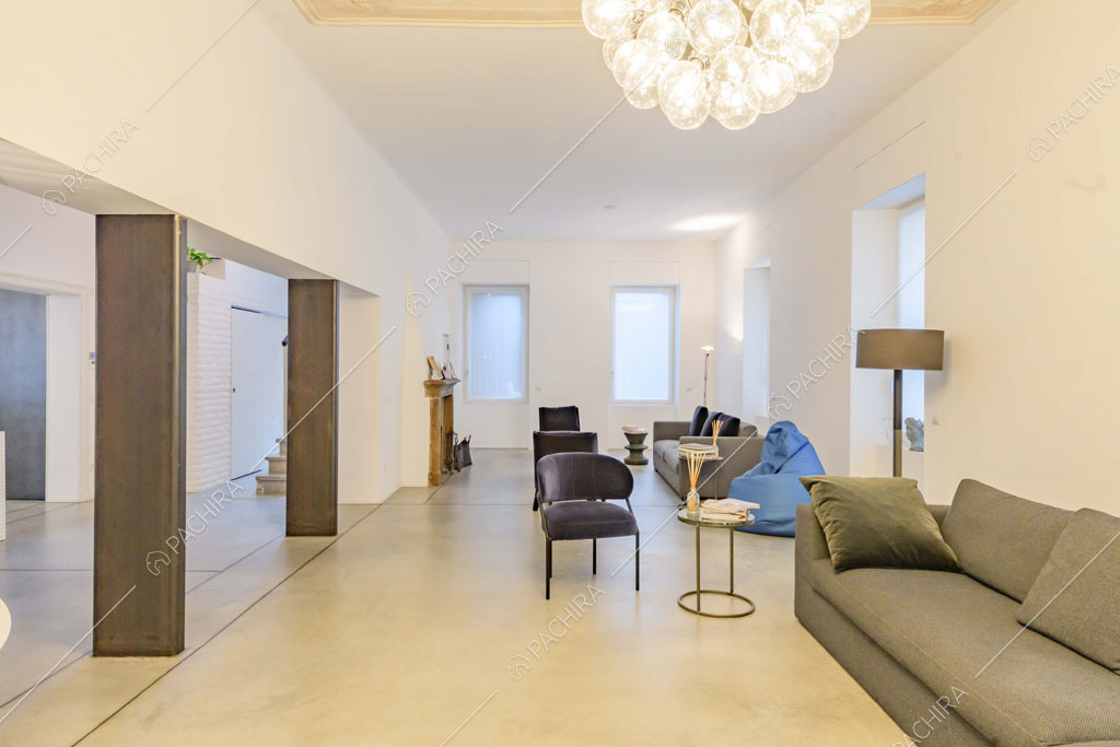 Ampia zona living con pareti e soffitto bianchi, lampadario di design e colonne in metallo a vista