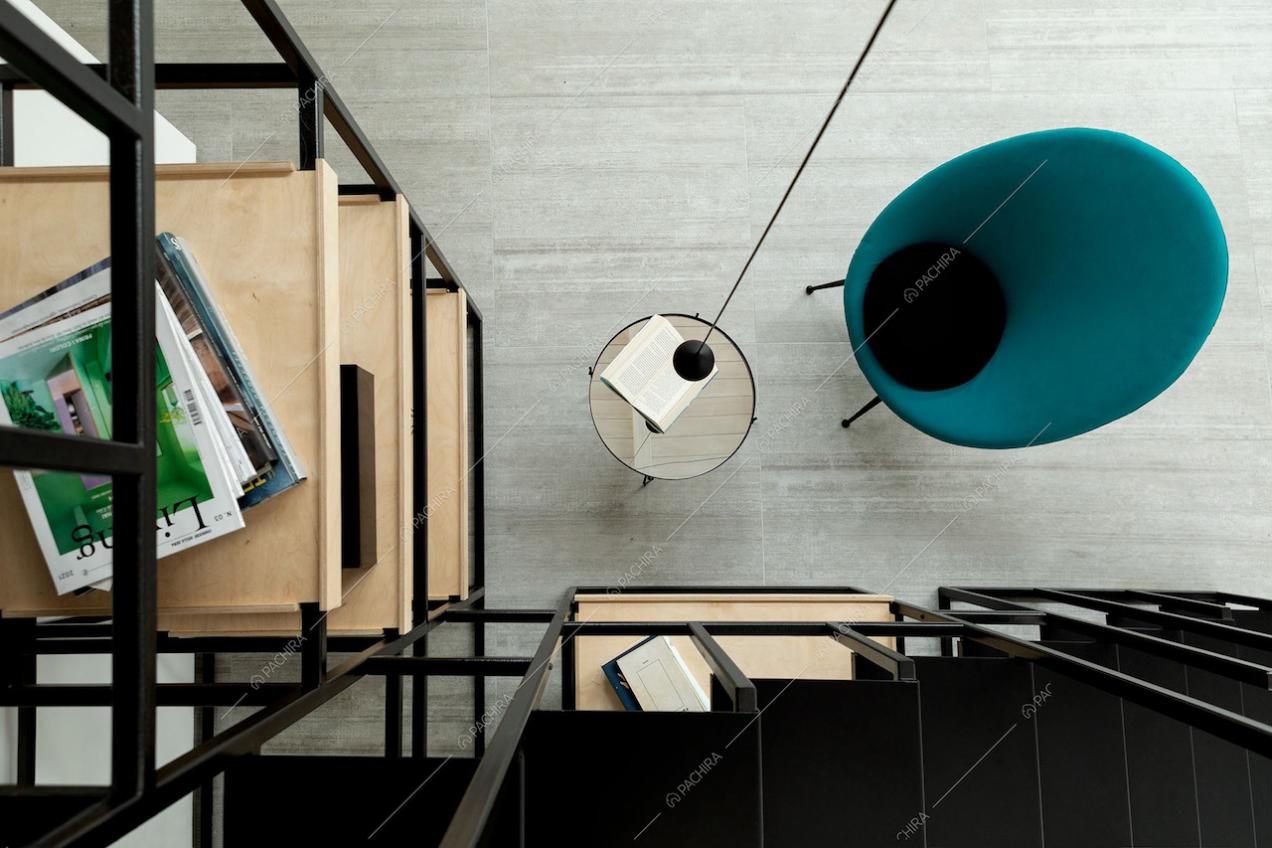 Dalle scale nere in metallo vista sui ripiani della libreria in legno e sul tavolino e poltrona di design