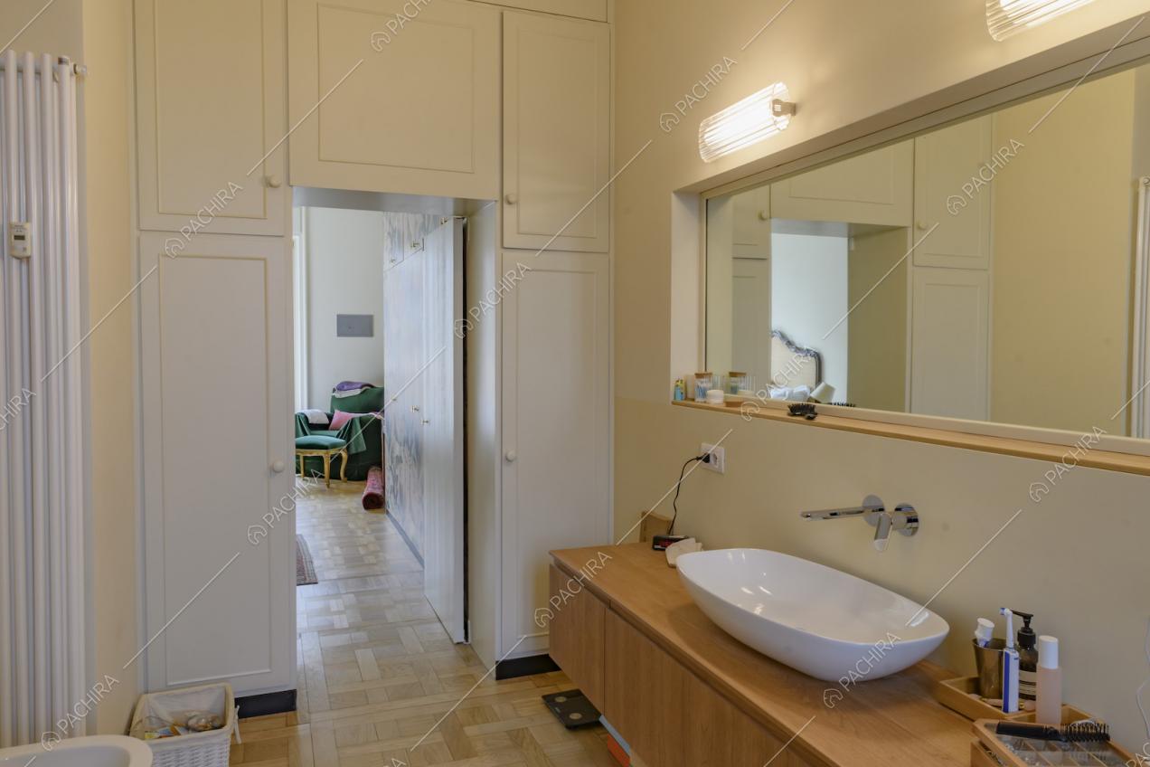 Bagno con pavimento in parquet, armadio bianco a muro e vista sulla camera da letto