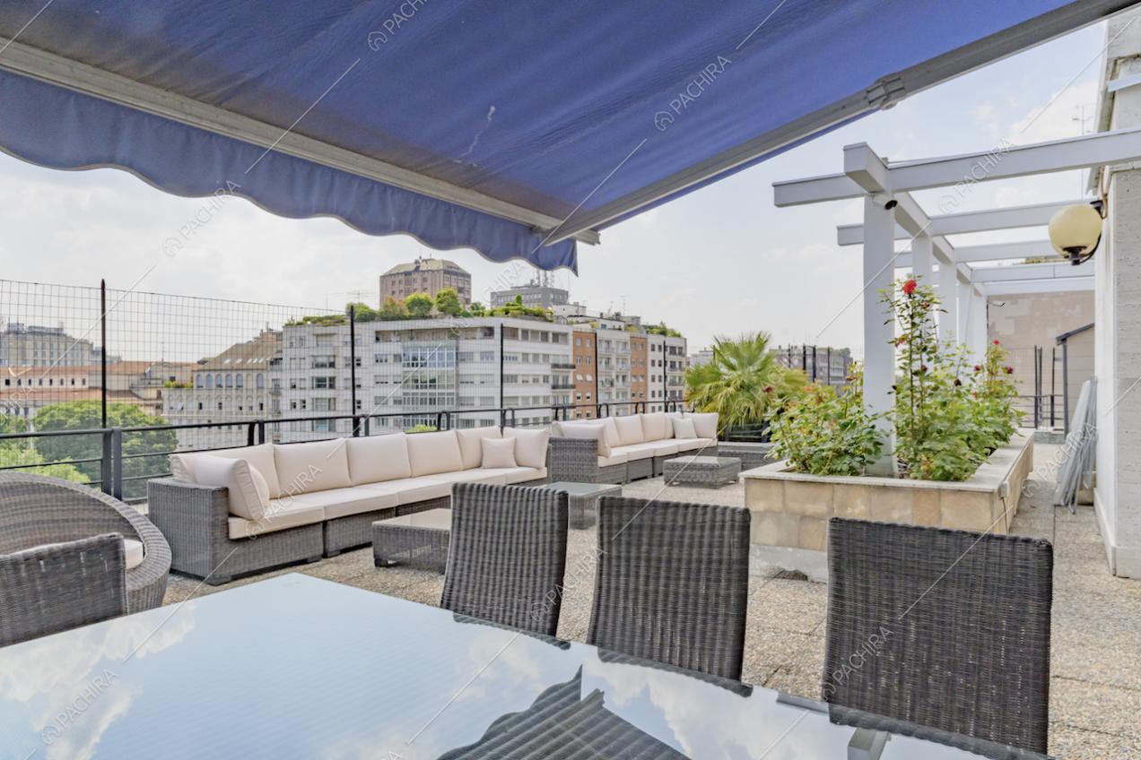 Tavolo da pranzo, riparato da un tendone blu, sulla terrazza con divani bianchi
