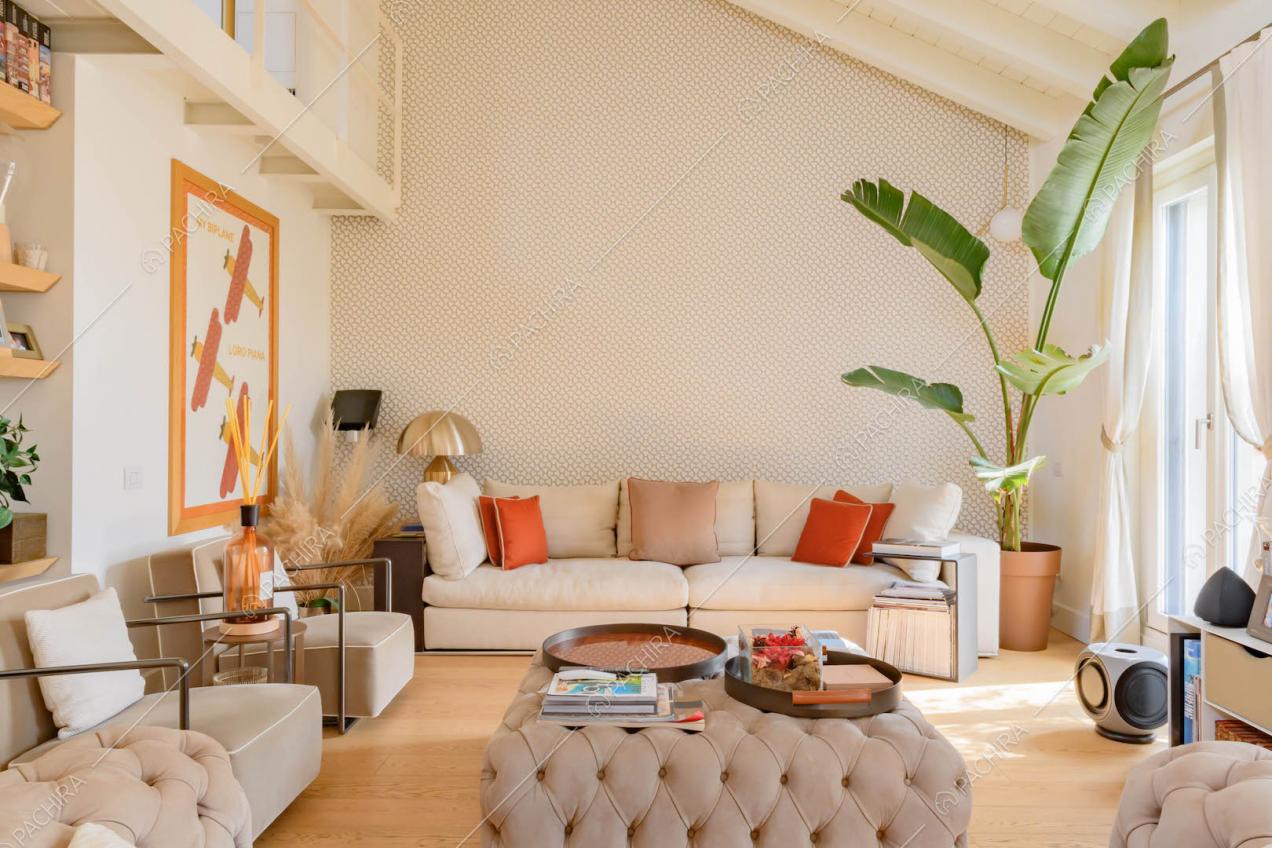 Divano e pouf beige nella zona living con pavimento in parquet e vetrate