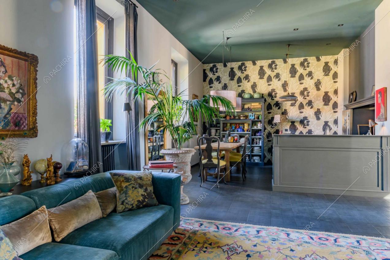 Sala con divano in velluto azzurro, carta da parati e cucina a vista