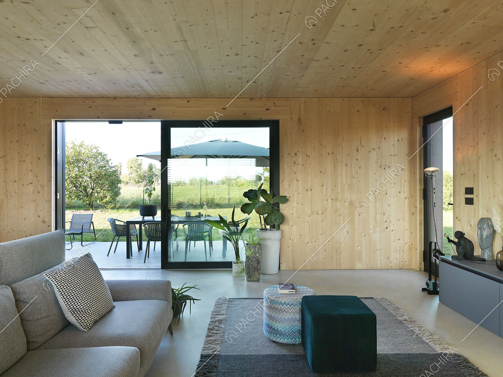 Dalla zona living con pareti e soffitto in legno, vista sul giardino tramite la porta-finestra