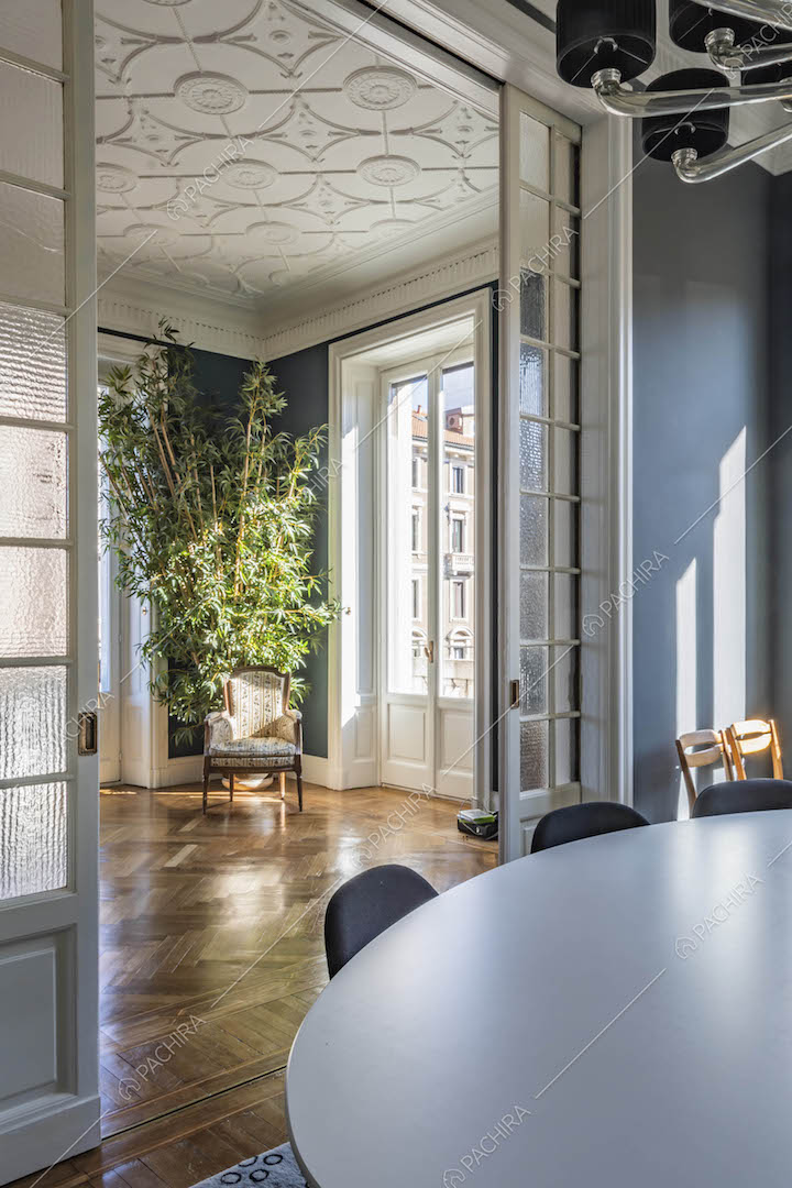 Porta a vetri bianca separa il salotto con boiserie sul soffitto dalla sala da pranzo
