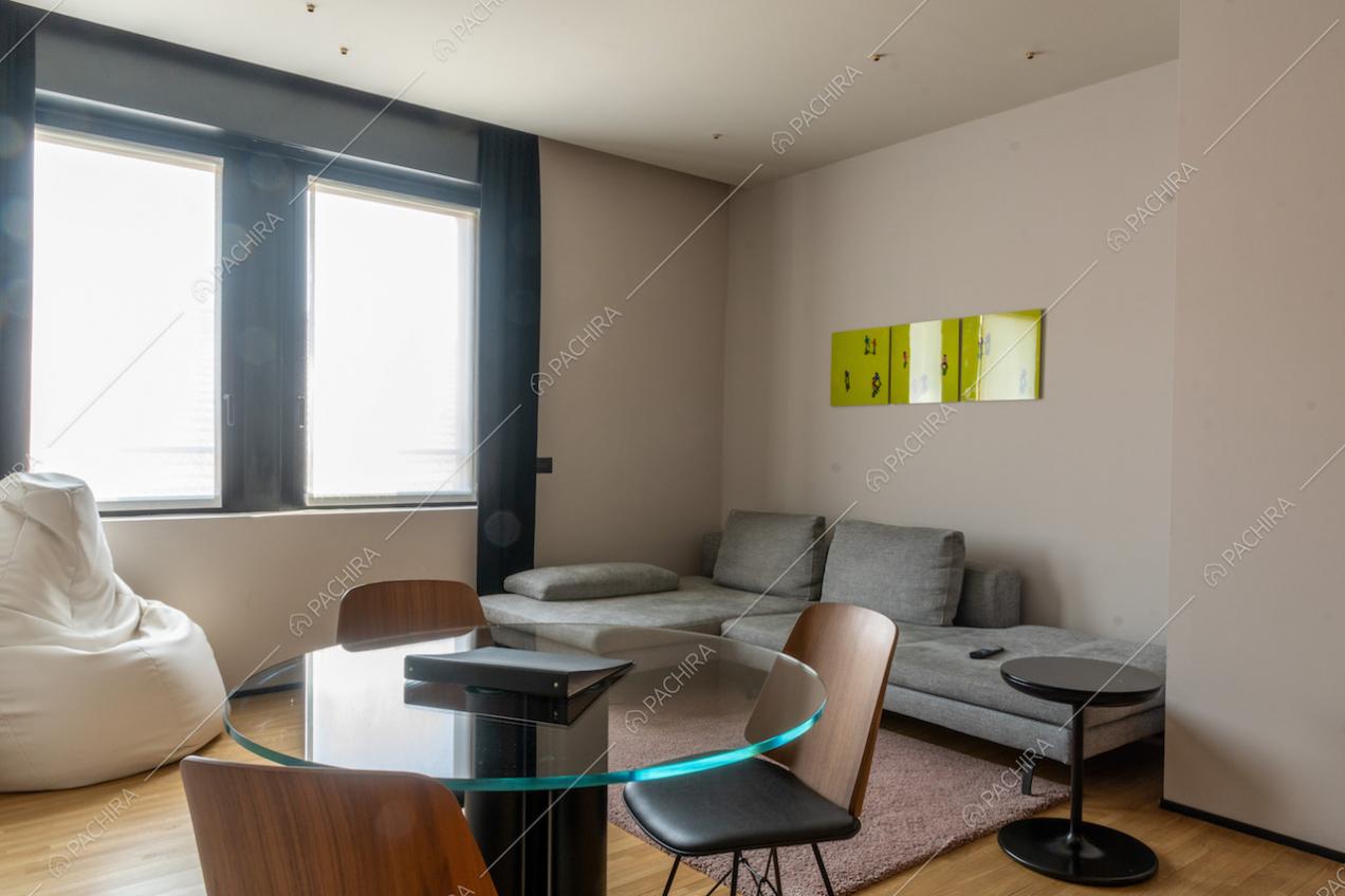 Sala con tavolo dal piano in vetro, divano angolare grigio e pavimento in parquet