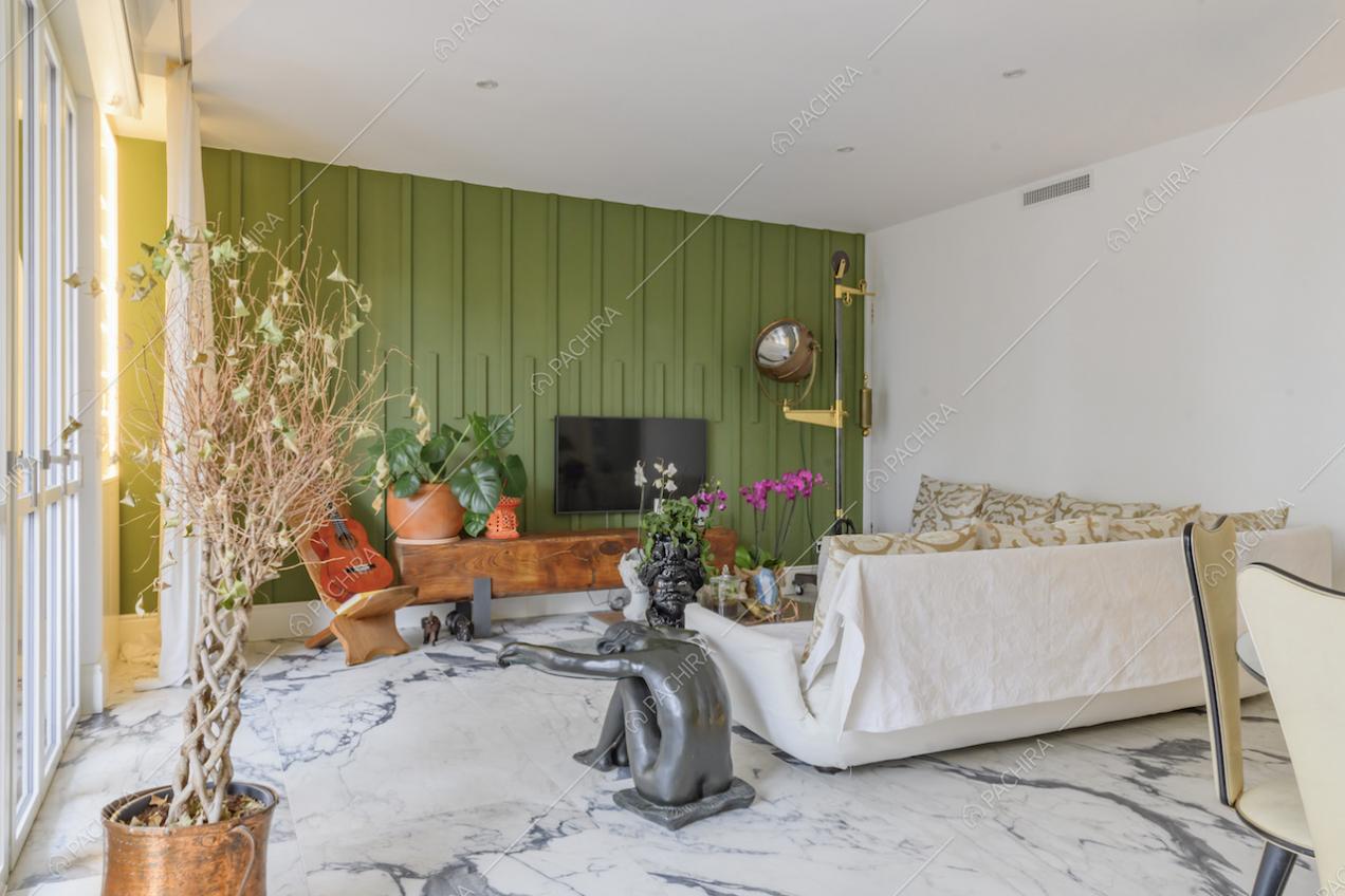 Luminoso salotto con parete verde con boiserie, divano bianco e tavolino con una statua come sostegno